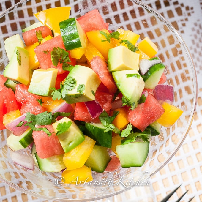 Salad of avocado, watermelon, cucumber, peppers, and red onions in glass bowl.