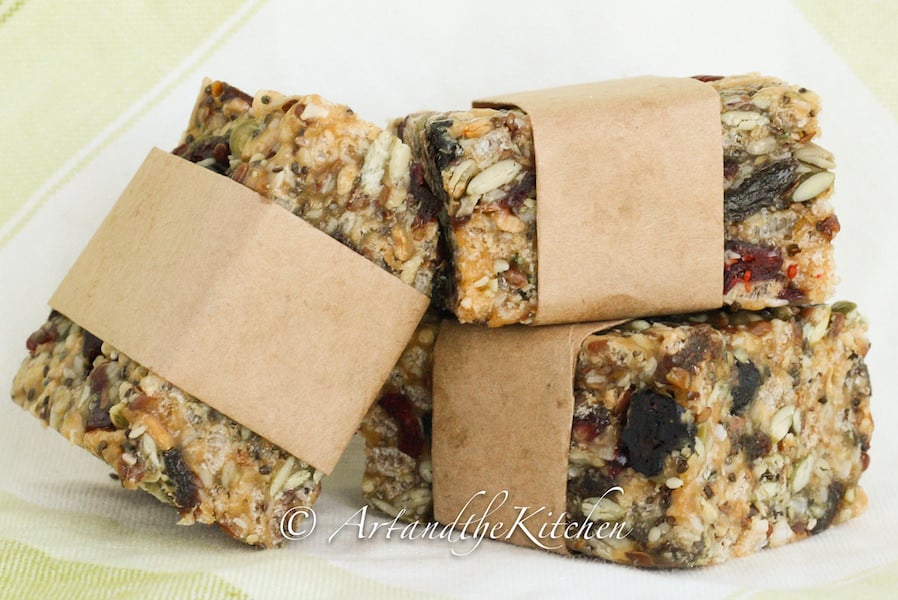 Three homemade protein bars wrapped in brown parchment paper loaded with seeds and dry fruit