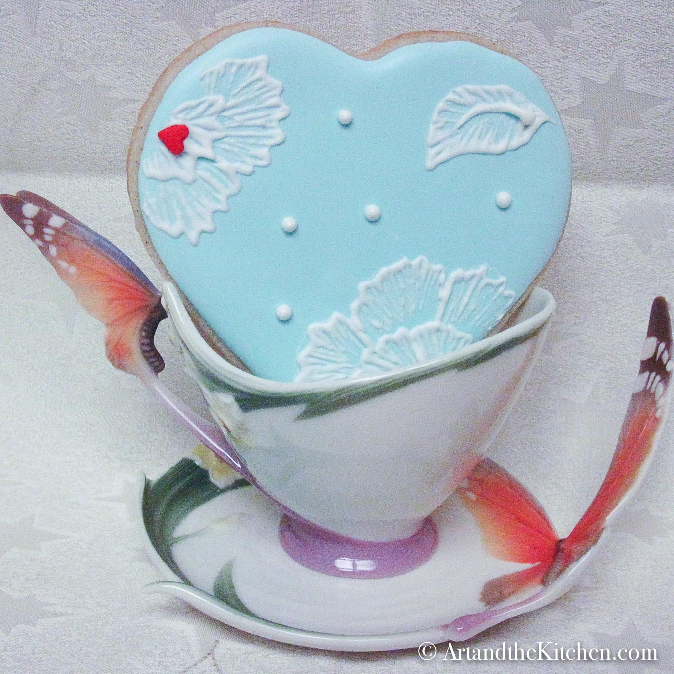 Blue heart shaped decorated cookie in decorative tea cup.