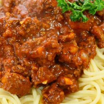 Thick meat sauce on spaghetti pasta with parsley sprig.