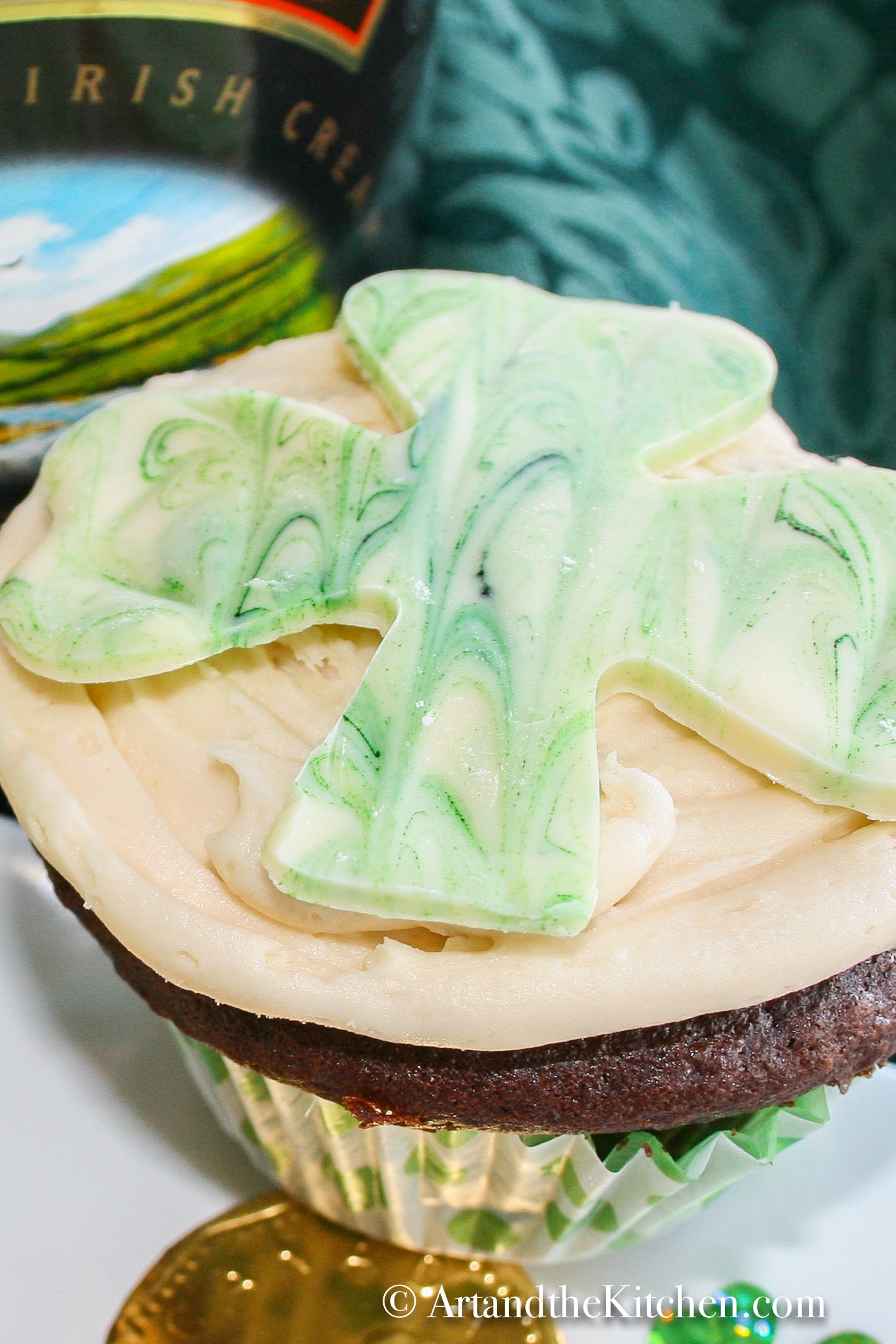 chocolate cupcake topped with a white chocolate shamrock. Baileys Irish cream bottle in background.