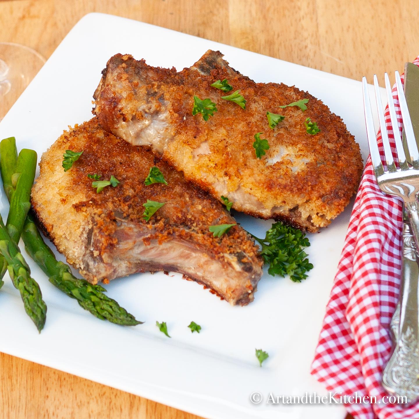 Two breaded chops fried golden brown and asparagus on square white plate. 