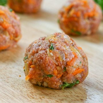 Uncooked meatballs made with ground turkey and vegetables on wood board.