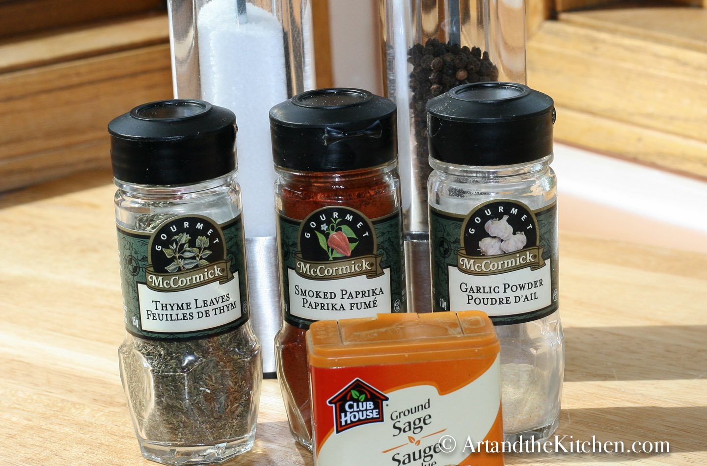 Bottles of spices, thyme, garlic powder, sage , smoked paprika with salt and pepper mills.