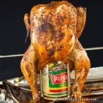 Grilled chicken inserted into a can of beer on beer can chicken holder.