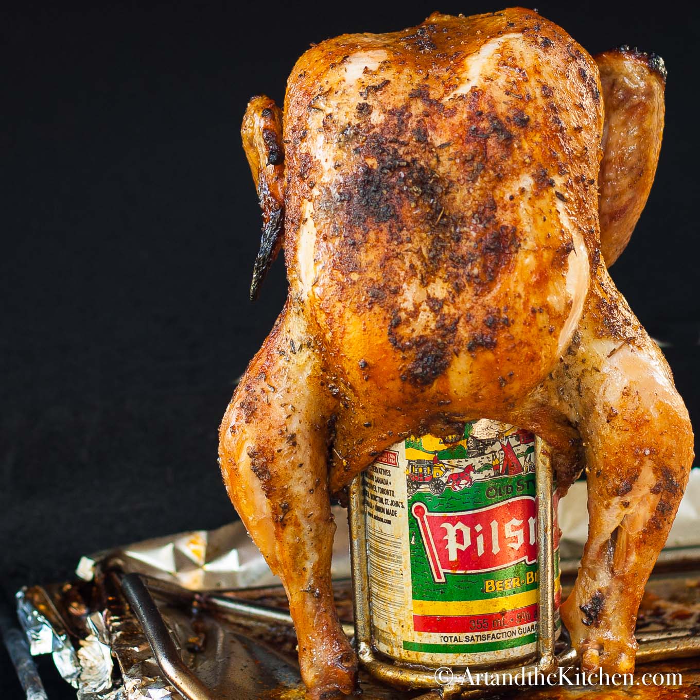 Barbecue roasted chicken inserted into a can of beer on a can roaster rack.