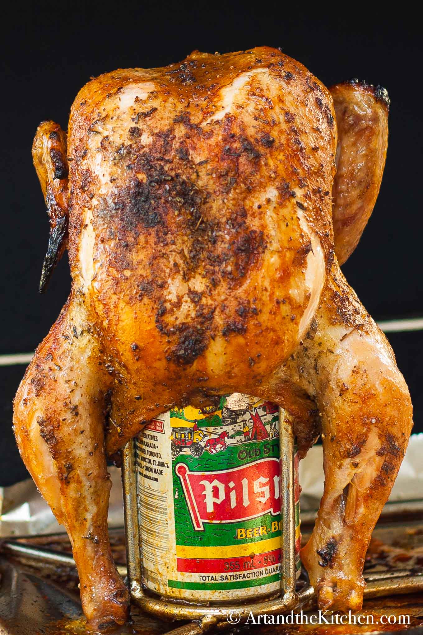 Barbecue roasted chicken inserted into a can of beer on a roaster rack.