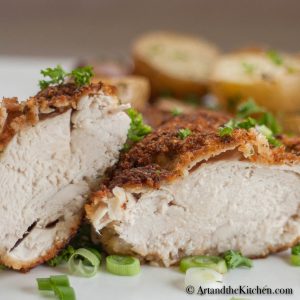 Chicken breast cut in half on white plate garnished with green onion slices.