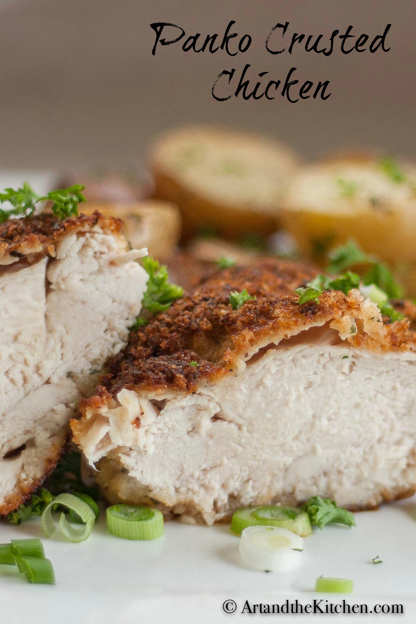 Chicken breast crusted with panko bread crumbs, cut in half on white plate garnished with green onion slices.