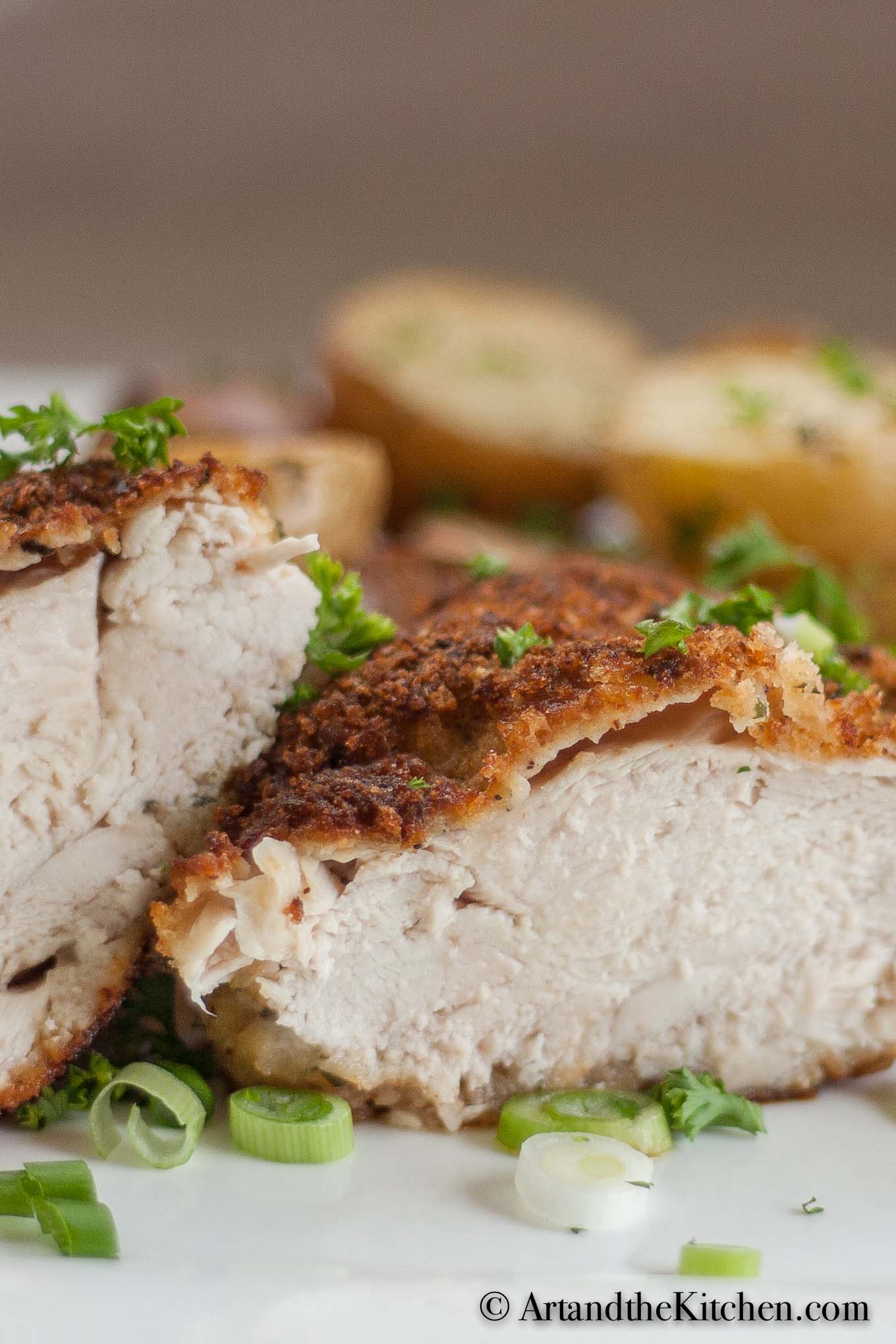 Chicken breast cut in half on white plate garnished with green onion slices.