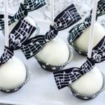 White chocolate coated cake pops with music themed ribbon tied to stick.