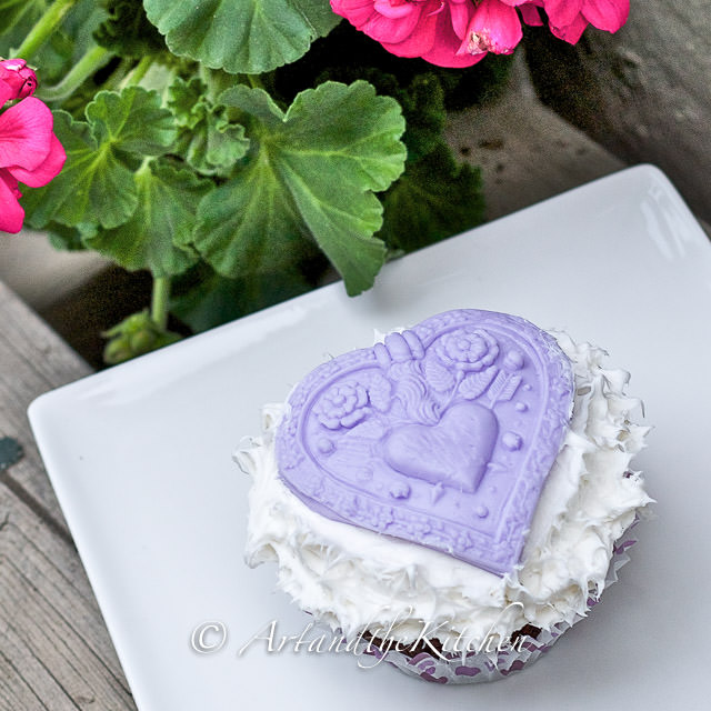 Cupcake with white buttercream frosting topped with purple fondant heart.