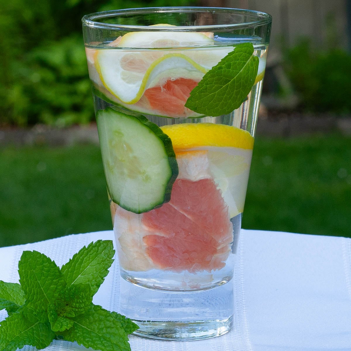 A tall glass of water infused with cucumber, lemon, grapefruit slices, and mint leaves.