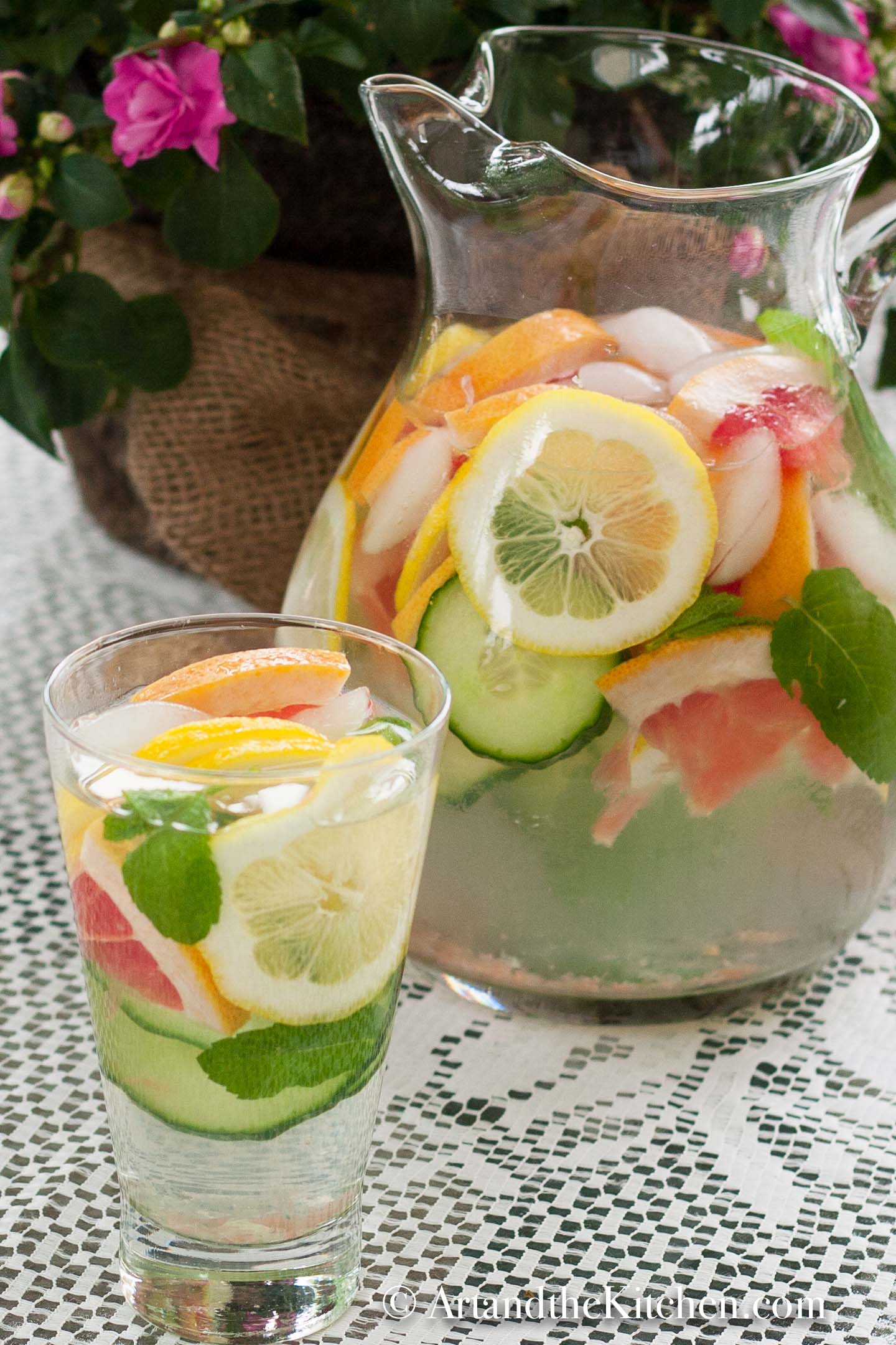 Glass pitcher and glass of water with slices of grapefruit, cucumber, lemon and mint.