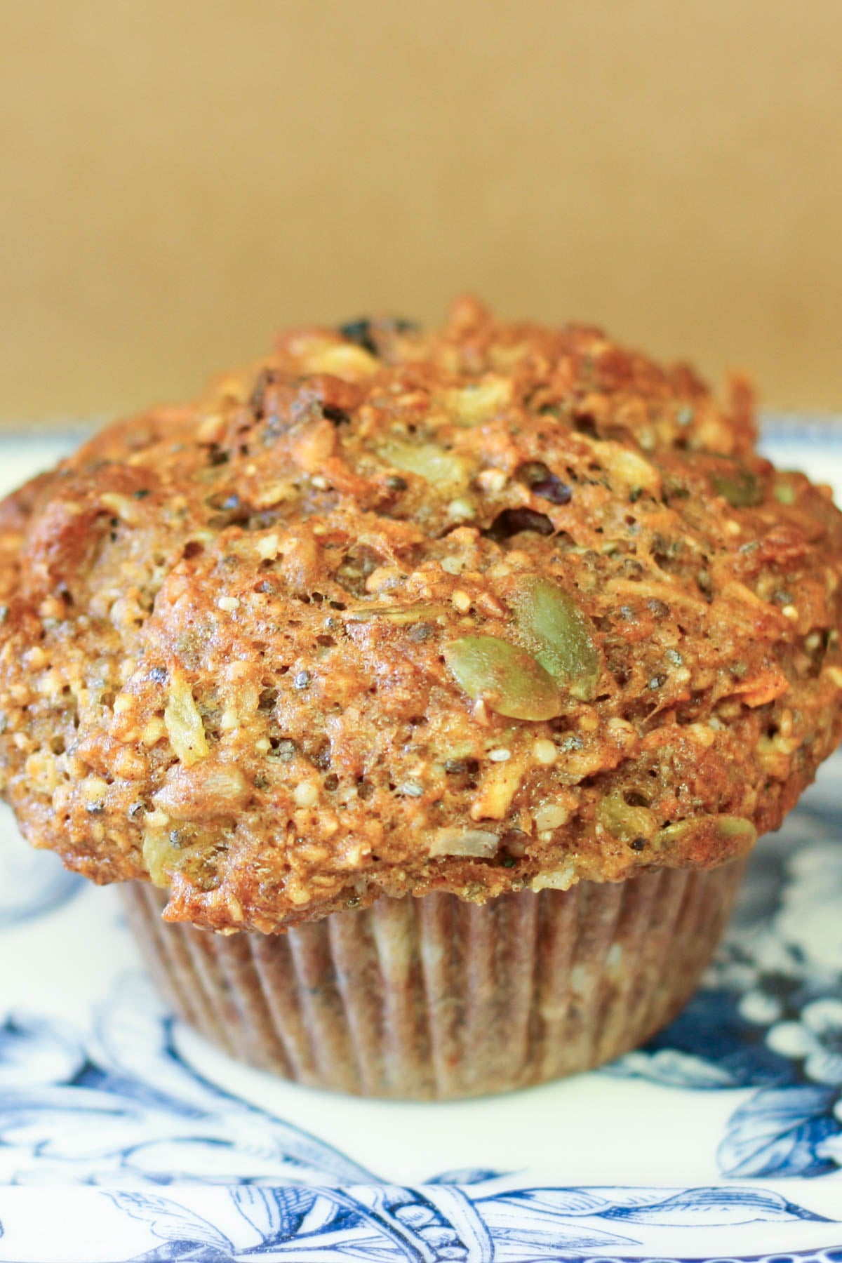 Whole grain muffin with nuts and seeds on a blue floral plate. The muffin has a golden-brown top and a rustic, hearty texture.