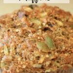 Whole grain muffin with nuts and seeds on a blue floral plate. The muffin has a golden-brown top and a rustic, hearty texture.