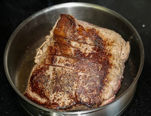 Roast beef searing in stainless steel skillet.