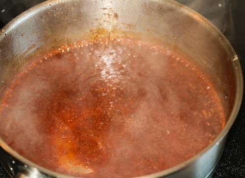 Beef broth glaze simmering in stainless steel skillet.