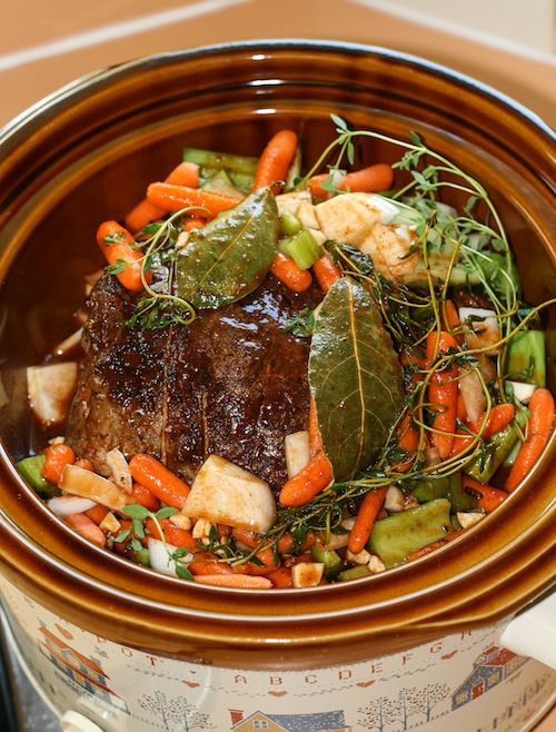 Roast beef with vegetables and herbs in a slow cooker.