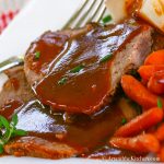 Slices of roast beef covered in gravy with a side of carrots.