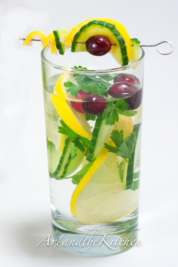 Tall glass of water and cucumber, lemon slices, parsley and cilantro.