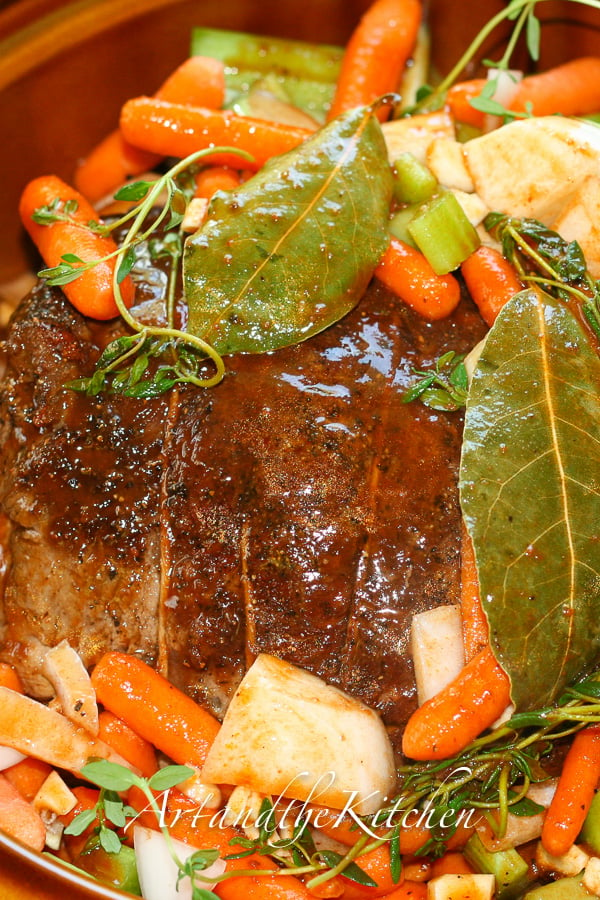 Roast beef in slower cooker with vegetables and herbs.