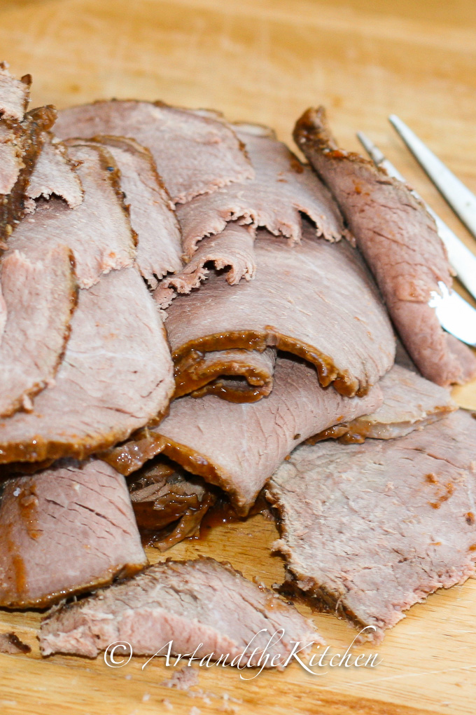 Slices of cooked roast beef on wood cutting board.