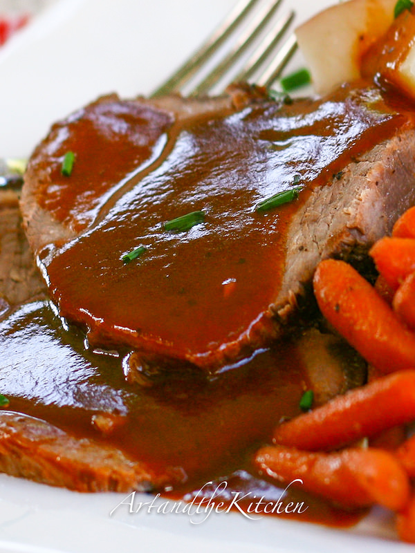 Slices of roast beef covered with a rich gravy and side of carrots.