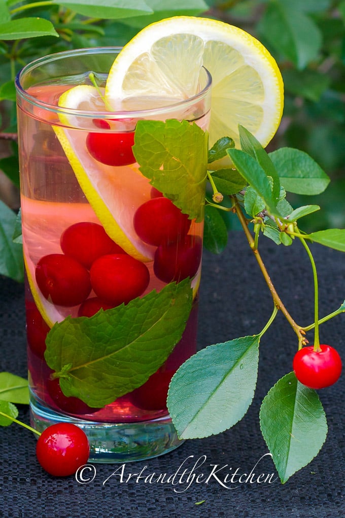 Tall glass filled with water infused with sour cherries and lemon slices.