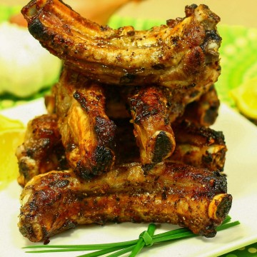 Stack of Greek marinated ribs with green onion sprigs and lemon slices