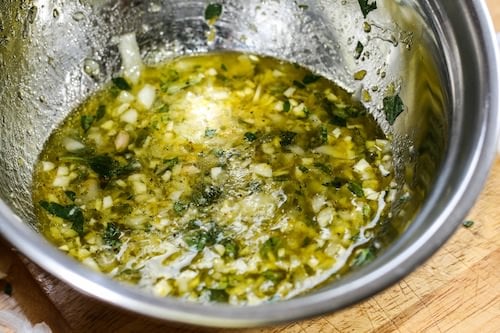 Stainless steel bowl with marinate of lemon, garlic, onions, oregano and olive oil.