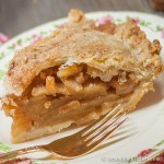 Slice of apple pie on decorative plate with gold plated fork.