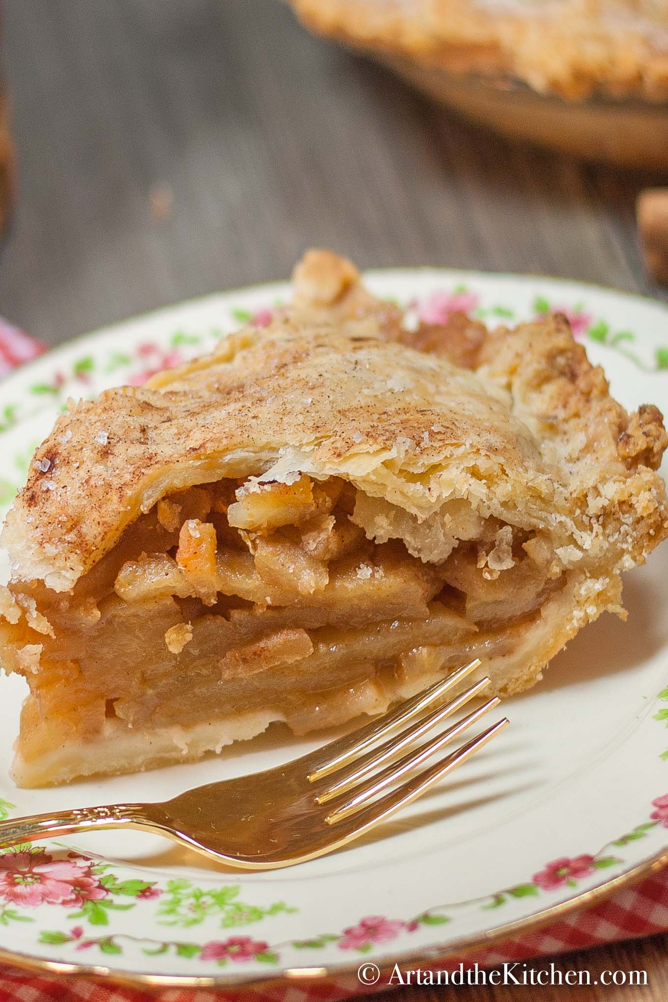 Slice of apple pie on decorative plate with gold plated fork.