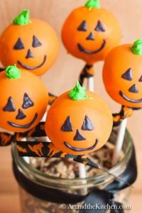 Five orange colored cake pops decorated like jack o lanterns displayed in a decorative jar.