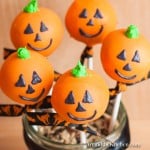 Five orange colored cake pops decorated like jack o lanterns displayed in a decorative jar.