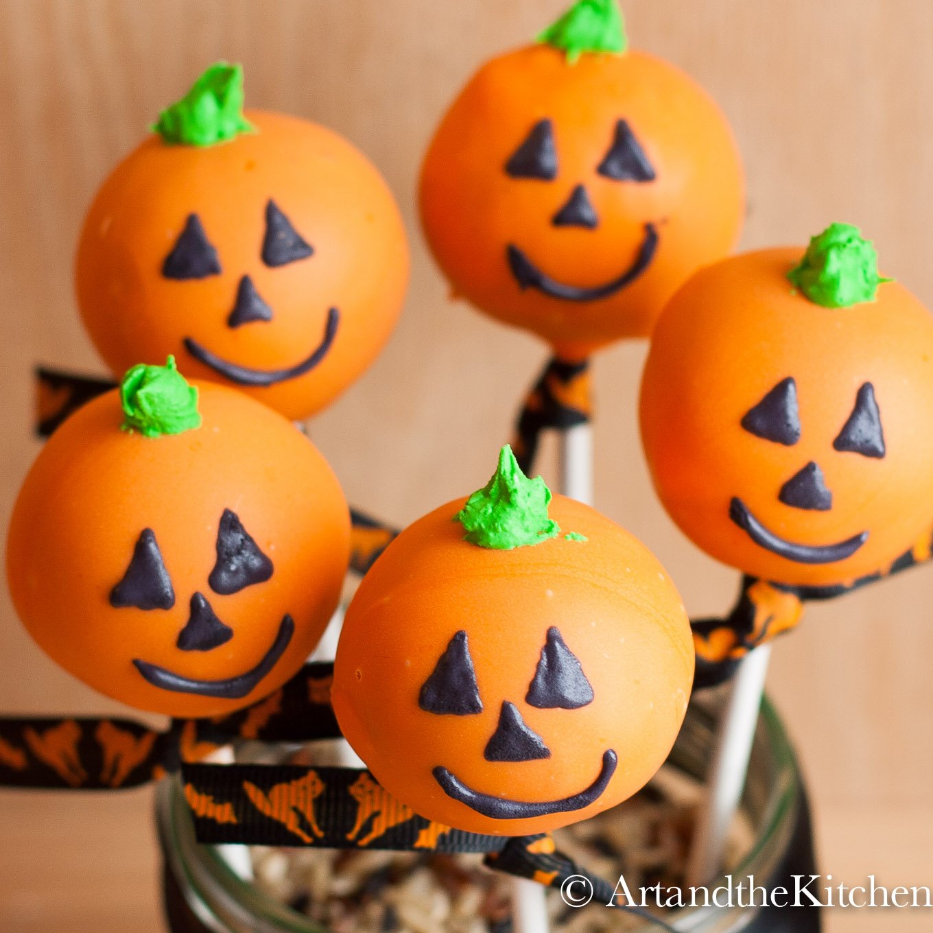 Five round cake pops that are decorated like Jack O Lanterns.