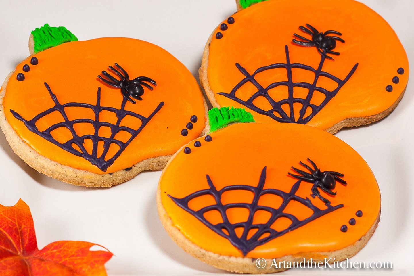 Pumpkin shaped sugar cookies decorated with orange icing and black spider web.