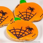 Pumpkin shaped sugar cookies decorated with orange icing and black spider web.