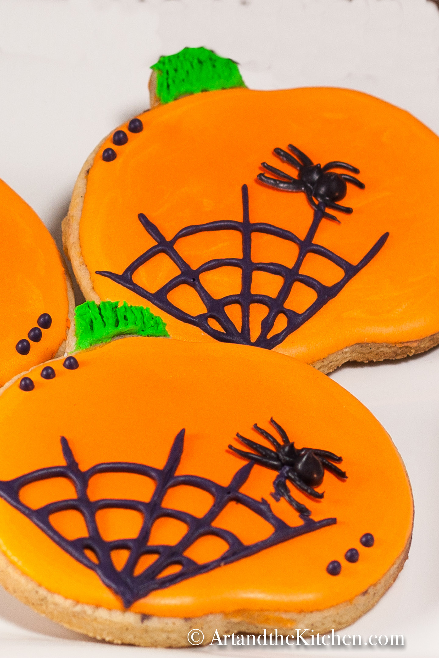 Pumpkin shaped sugar cookies decorated with orange icing and black spider web.