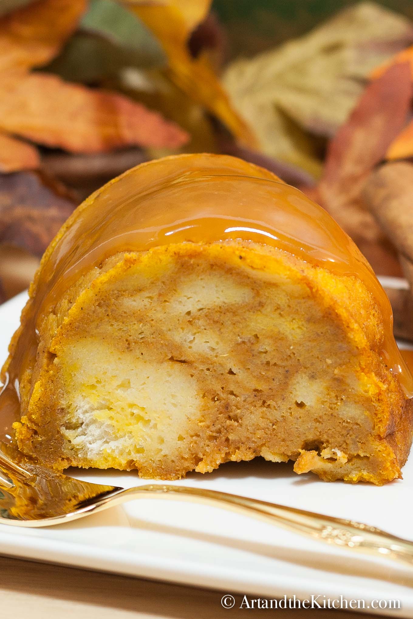 Slice of pumpkin flavored bread pudding covered with caramel sauce. Served on a white plate with gold fork.