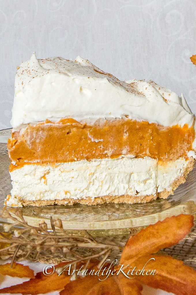 Slice of pumpkin pie with layers of pumpkin, cream cheese and whipped cream on amber coloured glass plate.