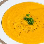 White bowl of squash soup garnish with cracked pepper and parsley.