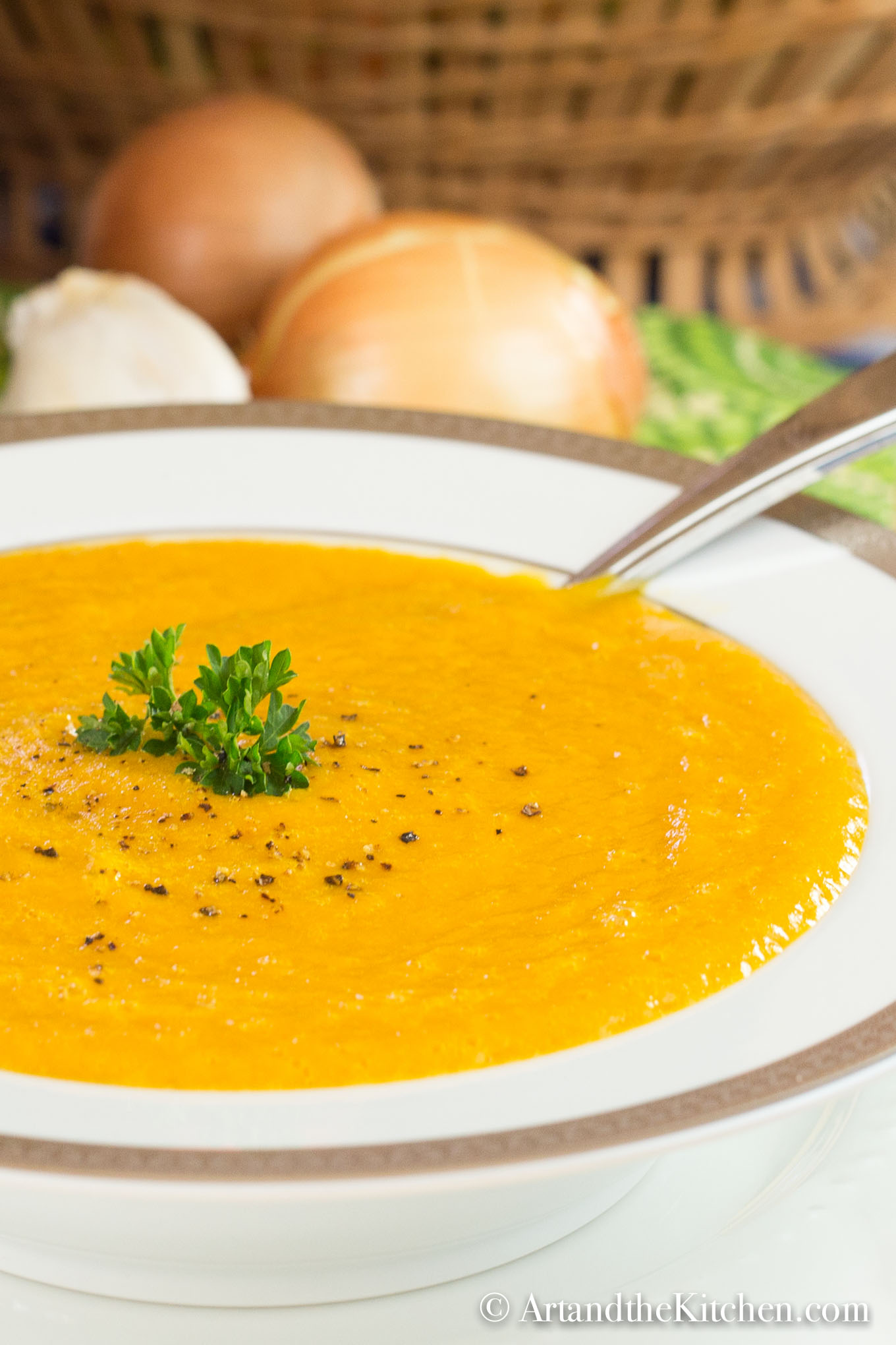 White bowl of squash soup garnish with cracked pepper and parsley.