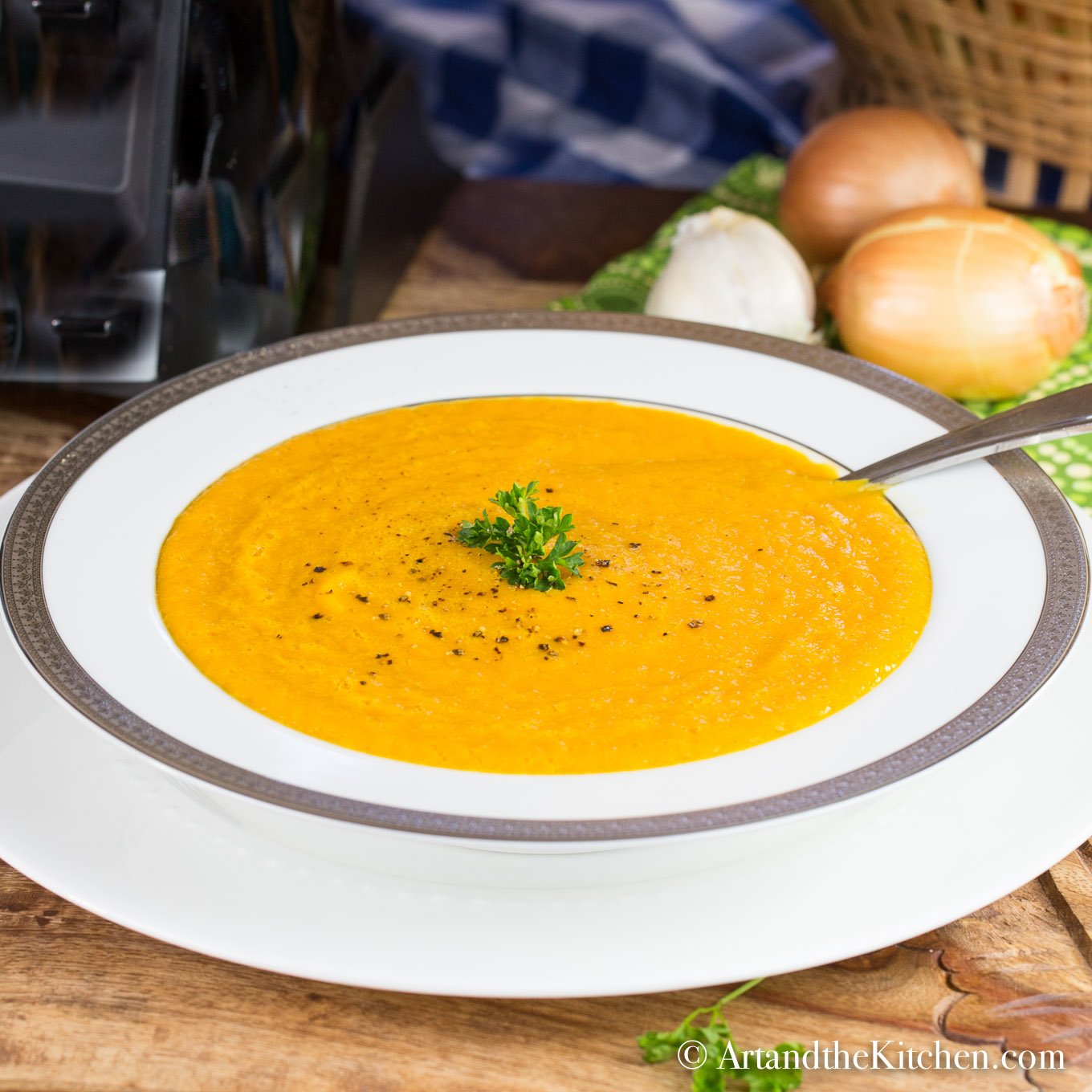 White bowl of squash soup garnish with cracked pepper and parsley.