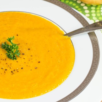 White bowl of squash soup garnish with cracked pepper and parsley.