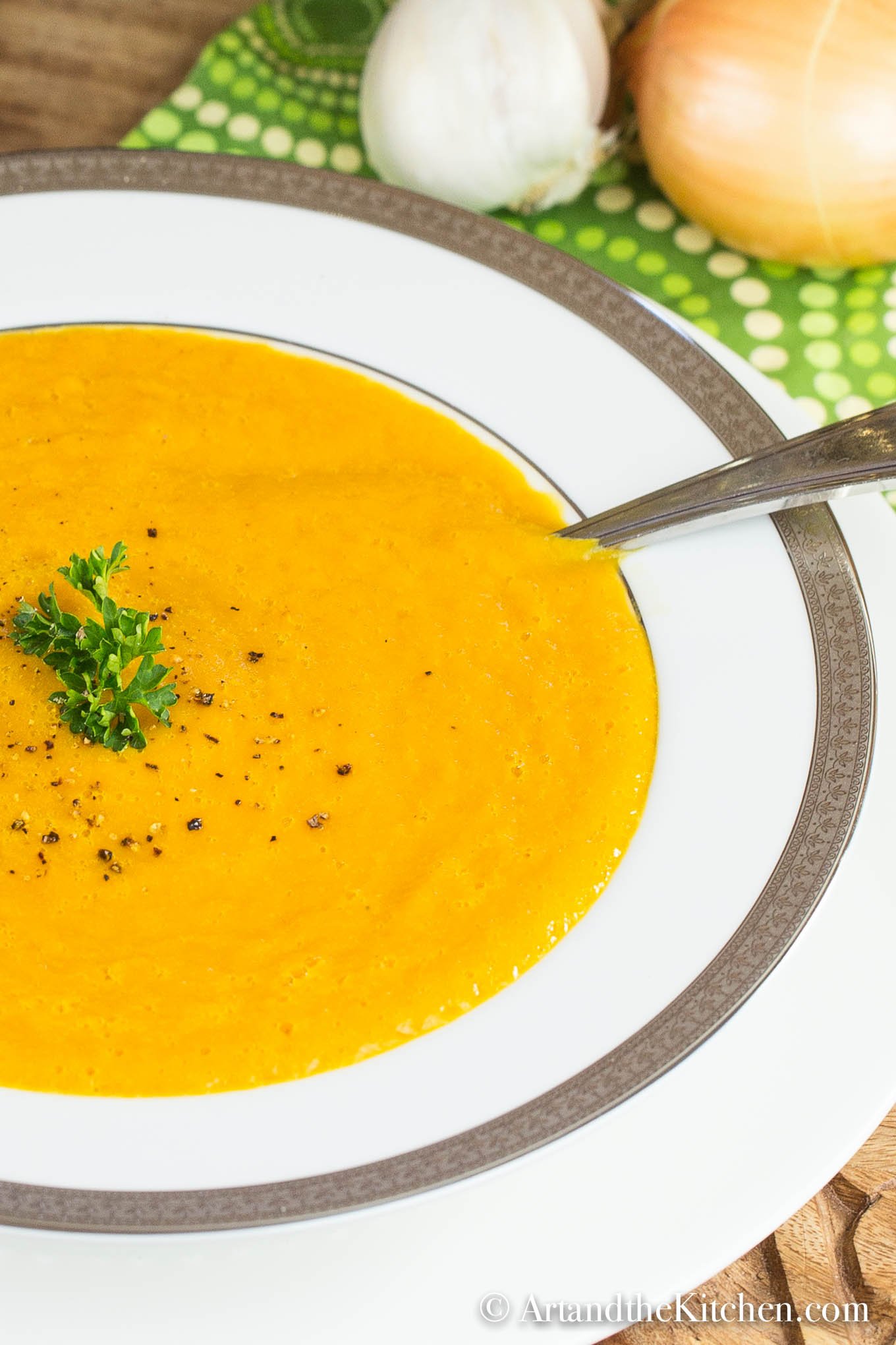 White bowl of squash soup garnish with cracked pepper and parsley.