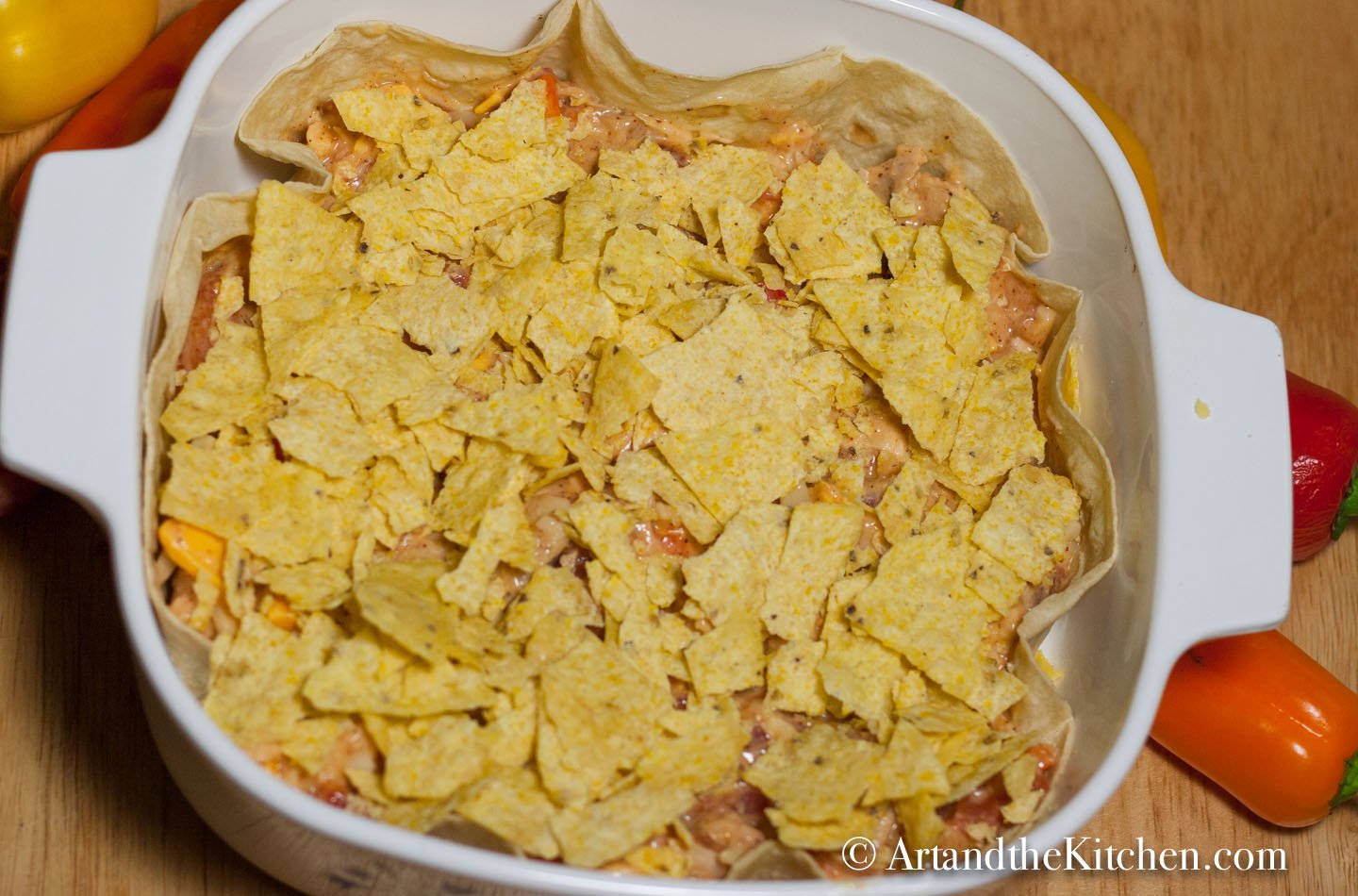 Square casserole dish with layers of unbaked tortillas, turkey mixture and topped with crushed tortilla chips.