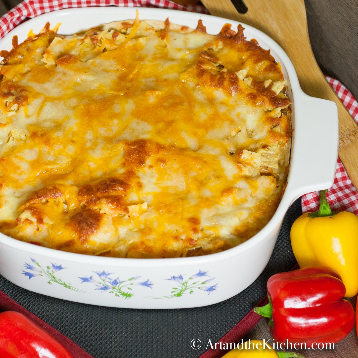 Square baking pan of casserole topped with a melted cheese . Yellow and red peppers by side of pan.