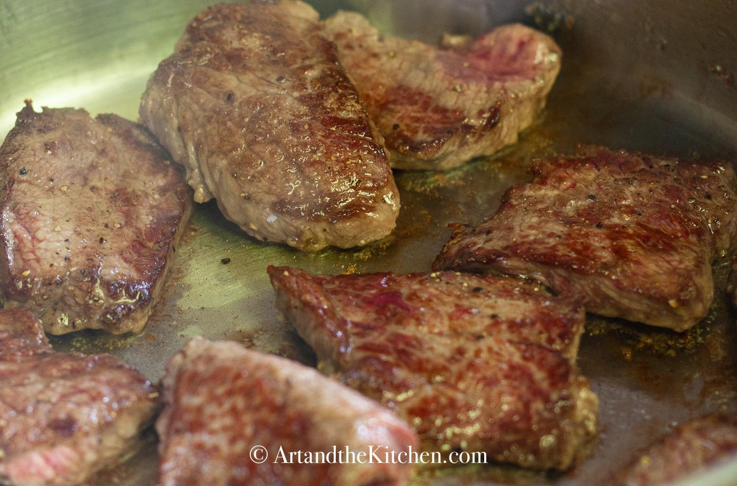 Beef searing in skillet.