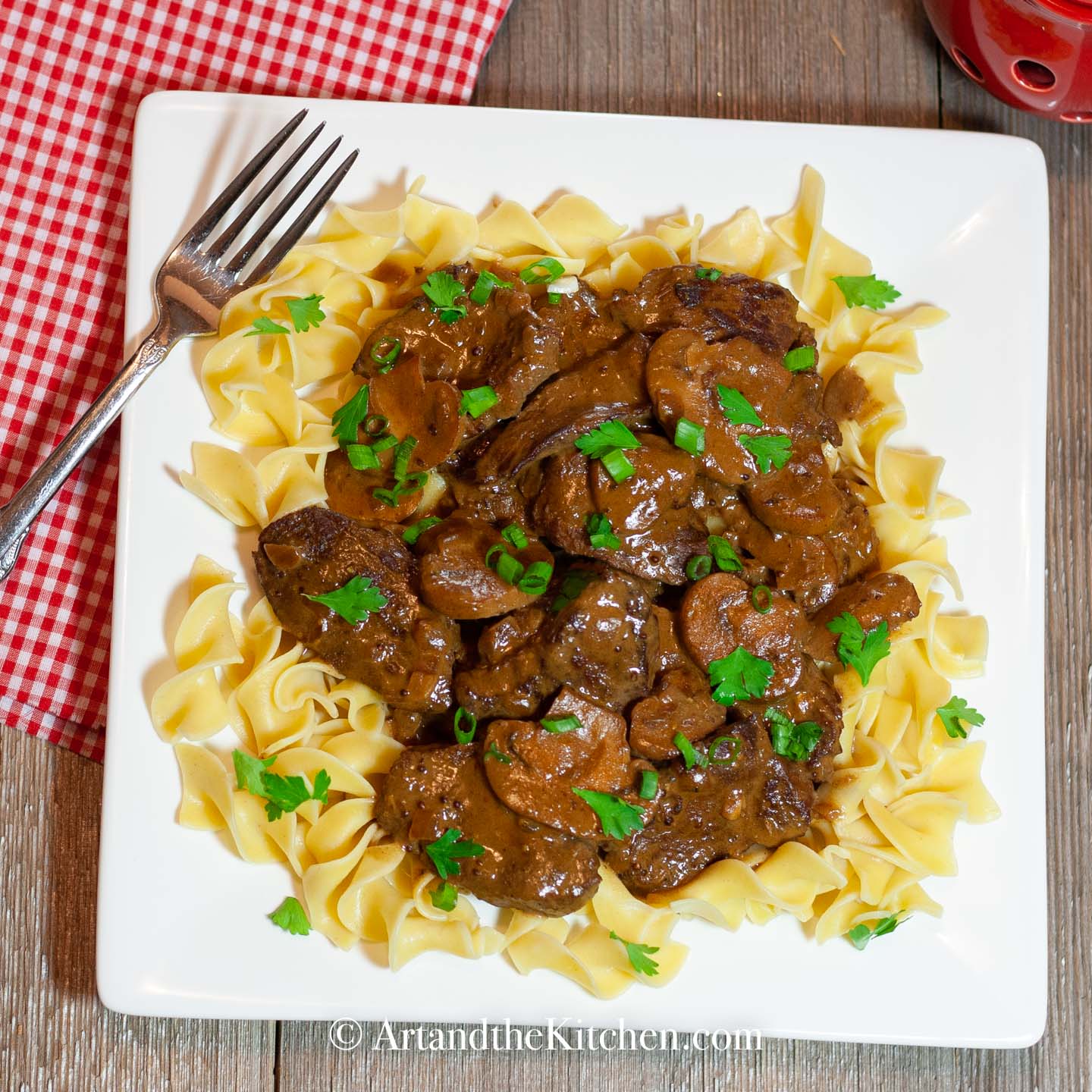 White square plate filled with beef stroganoff on a bed of broad noodles.